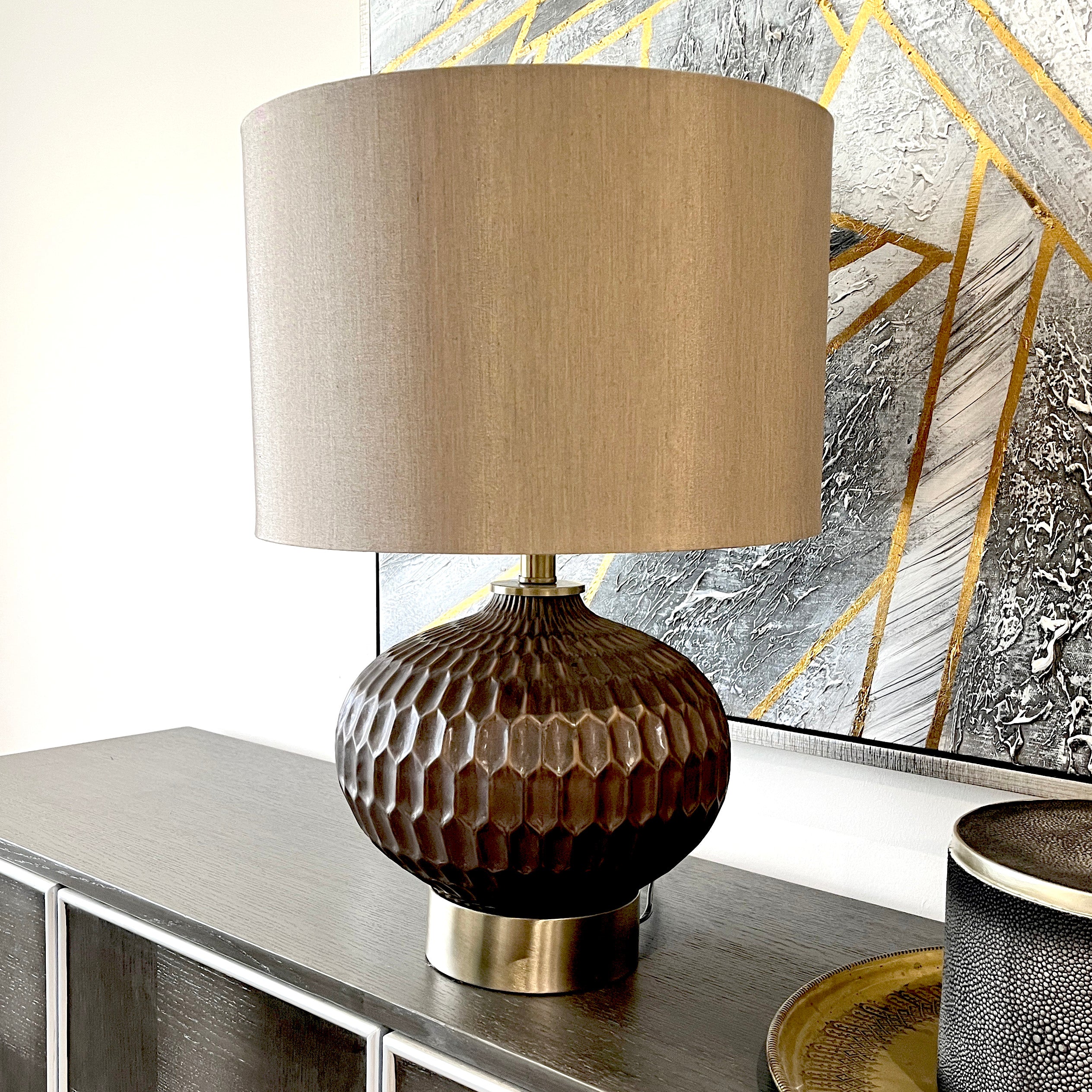 Table lamp with a textured brown base and beige shade on a decorative surface.