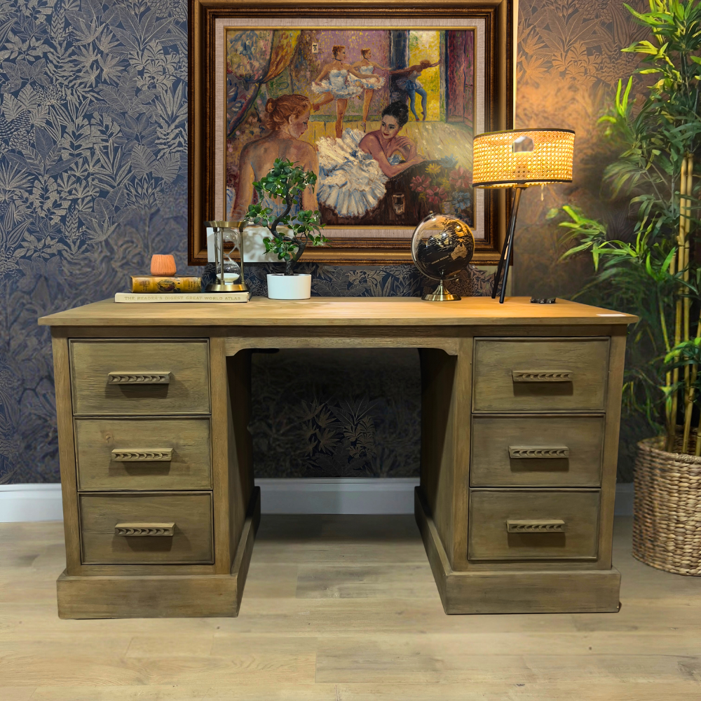 A wooden desk with six drawers, made from Mindi wood, MDF, and veneer, placed in an office setting with decorative items, a lamp, and a framed picture on the wall.