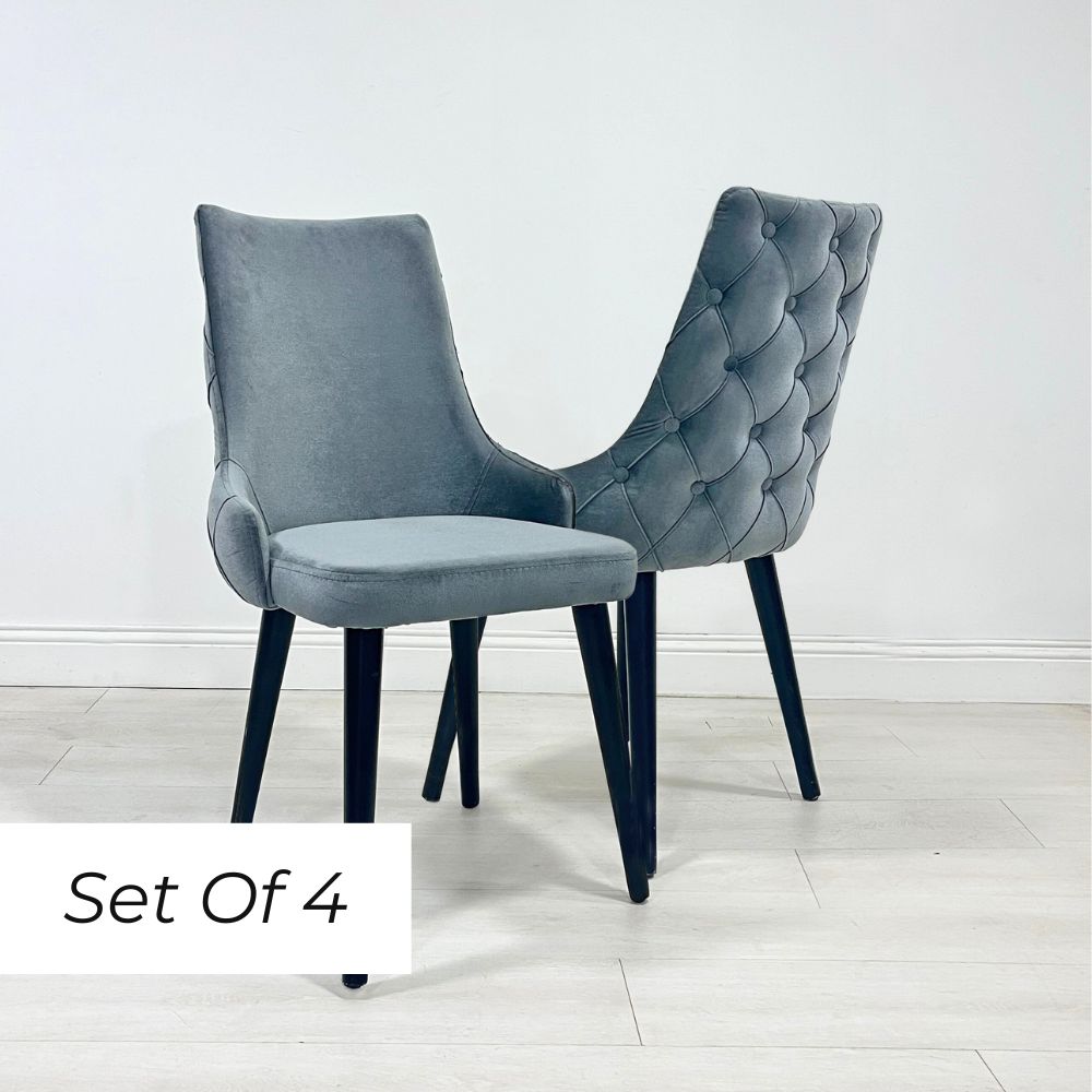 A set of four grey velvet dining chairs with button detailing and a scooped back design, displayed against a white background.