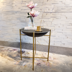 Small round table with gold legs against a stone wall.