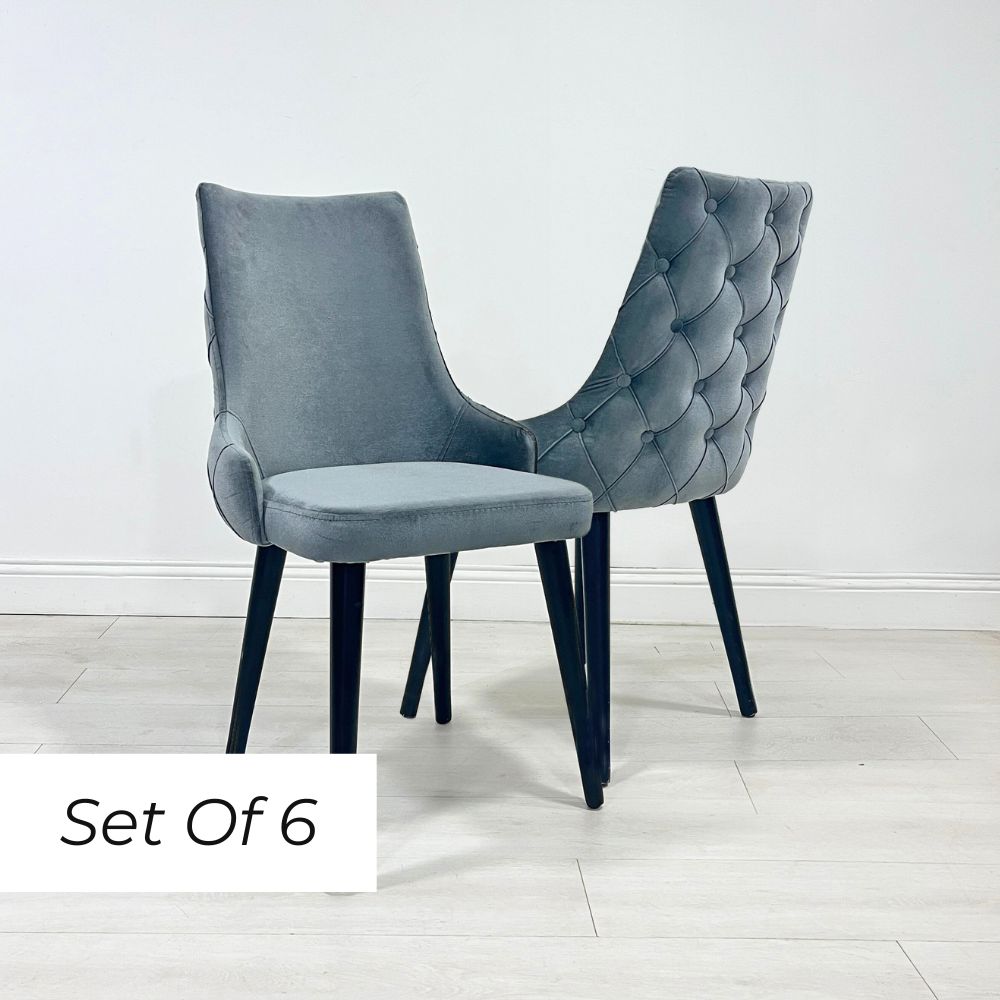 A set of six grey velvet dining chairs with button detailing and a scooped back design, displayed against a neutral background.