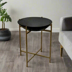 Round black table with gold legs in a room with a plant and sofa.