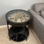 A round black side table with a built-in clock face design, featuring a modern minimalist frame and a lower shelf.