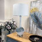 Decorative lamp on a wooden surface with a painting and flowers in the background