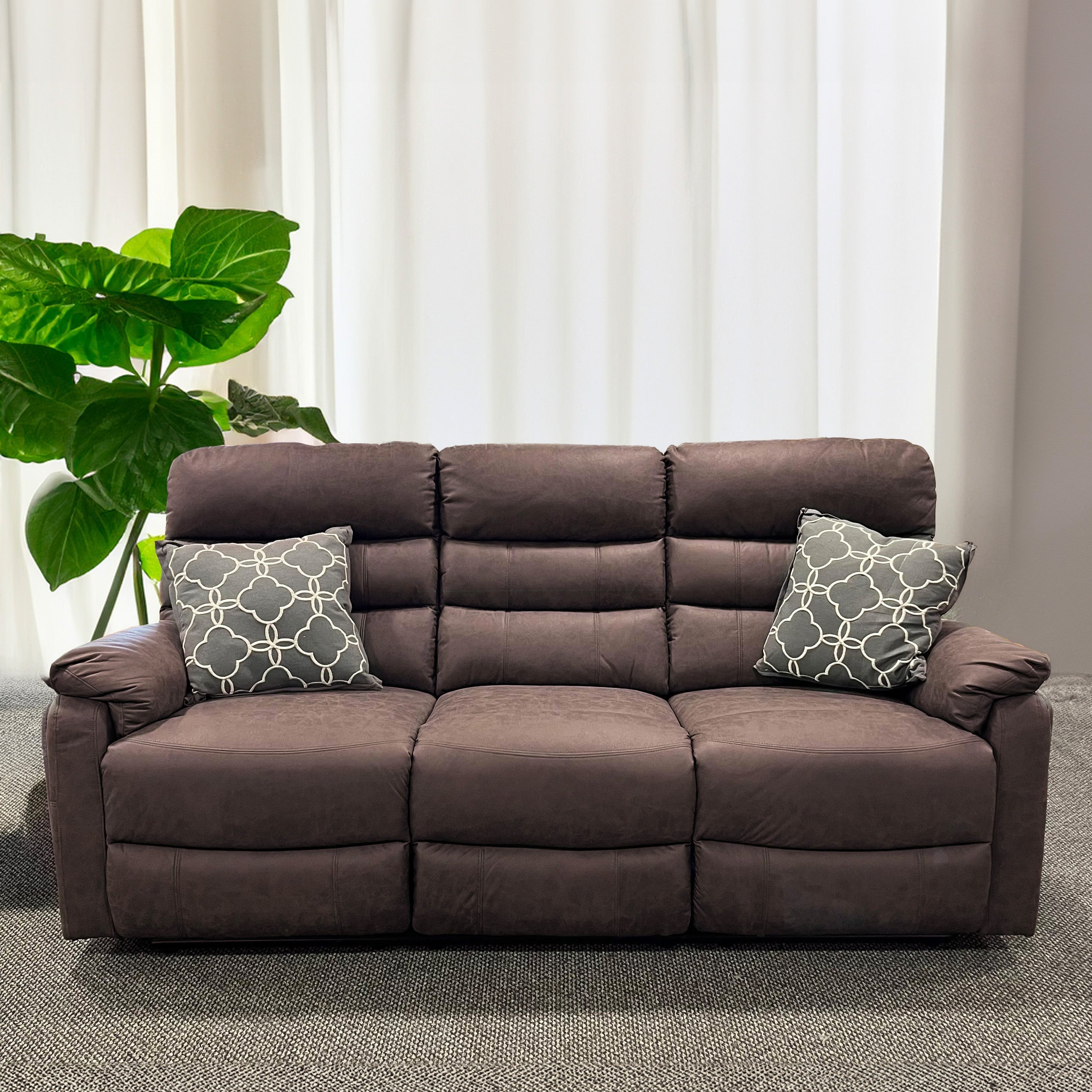 A brown leather 3-seater recliner sofa with two additional cushion seats, placed in a room with a large window and a green potted plant beside it.