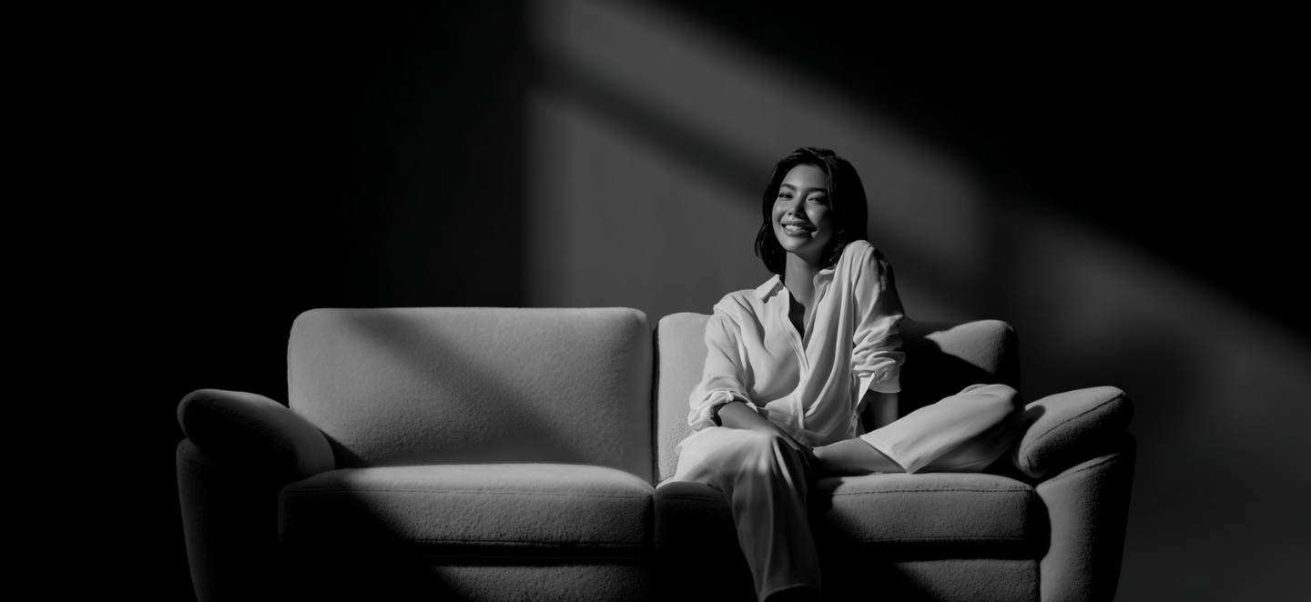 Woman sitting on a couch in a dimly lit room with soft shadows