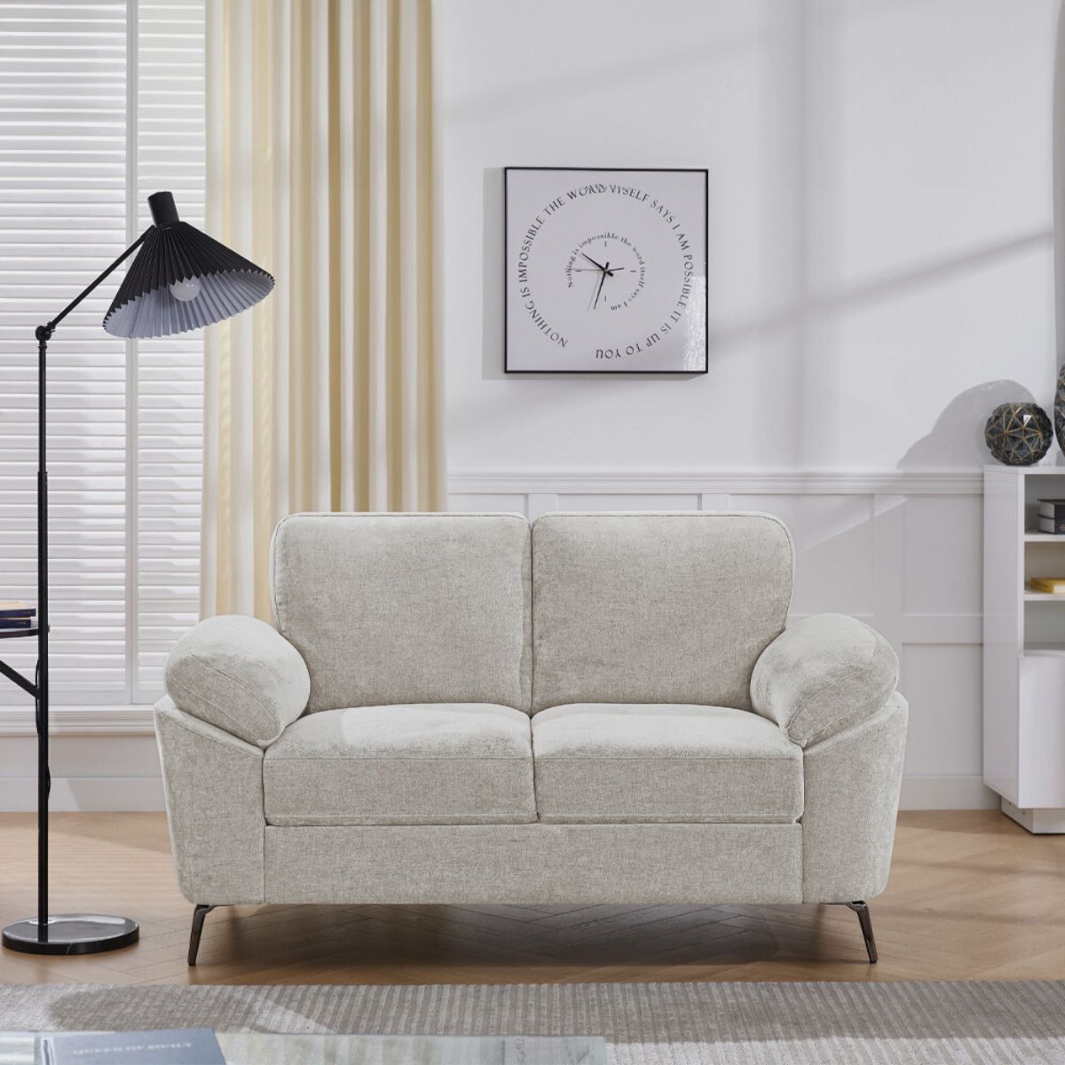 Beige loveseat in a living room setting with a lamp and wall art.