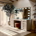 Bathroom vanity with large mirror and light bulbs, plant, and stool.